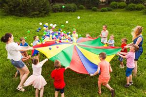 Camp counselors and kids bouncing balls on a colorful parachute